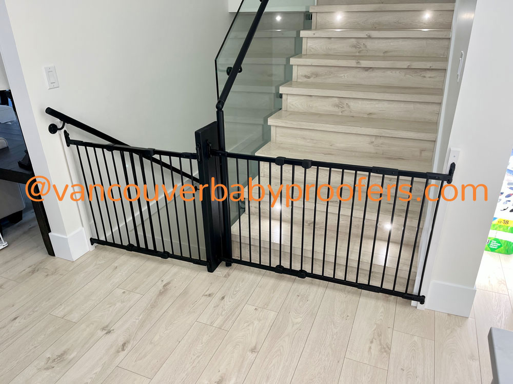 Black safety gate custom-fitted at the base of a glass-railing staircase in a Vancouver home